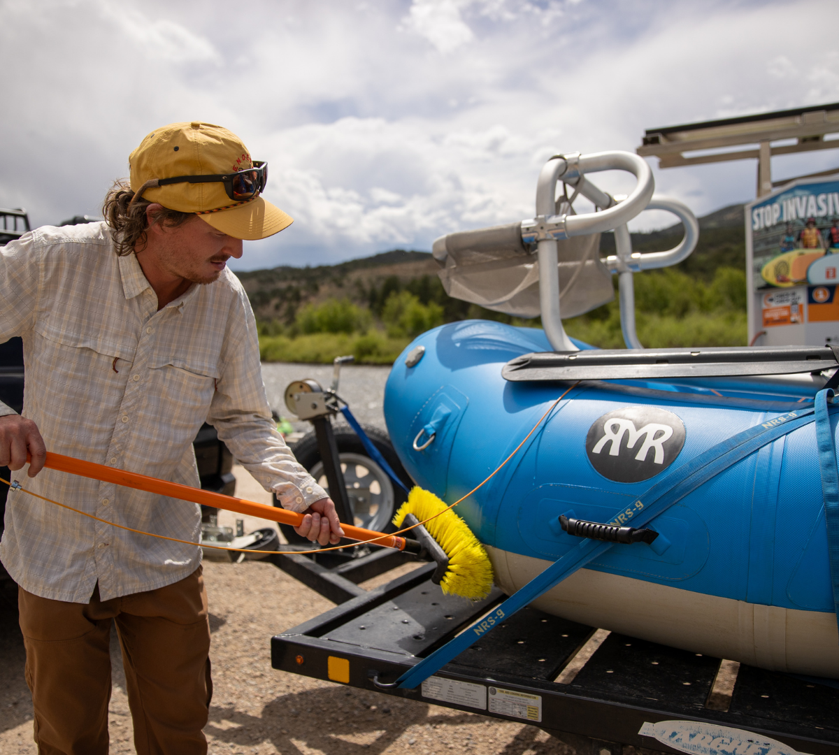 Person in yellow hat scrubbing a raft with a large cleaning brush