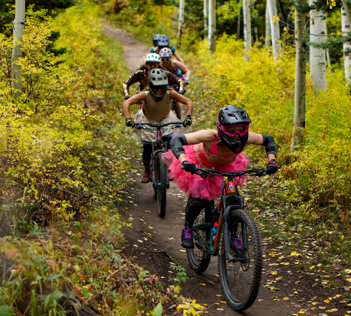 six women in prom dresses riding mountain bikes